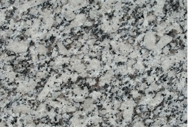 Amostra de granito Cinza Corumbá, fundo cinza-claro com salpicos pretos